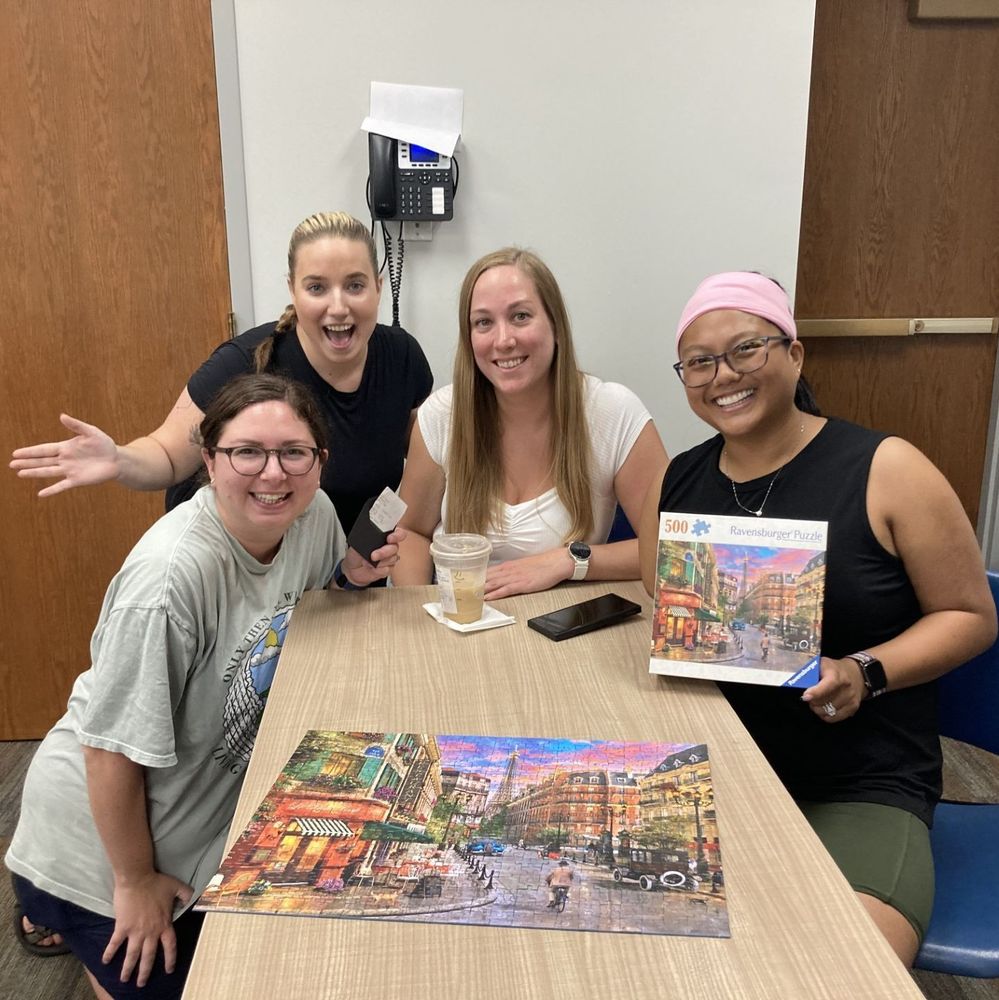Four women sitting and smiling. On the table is their completed puzzle.