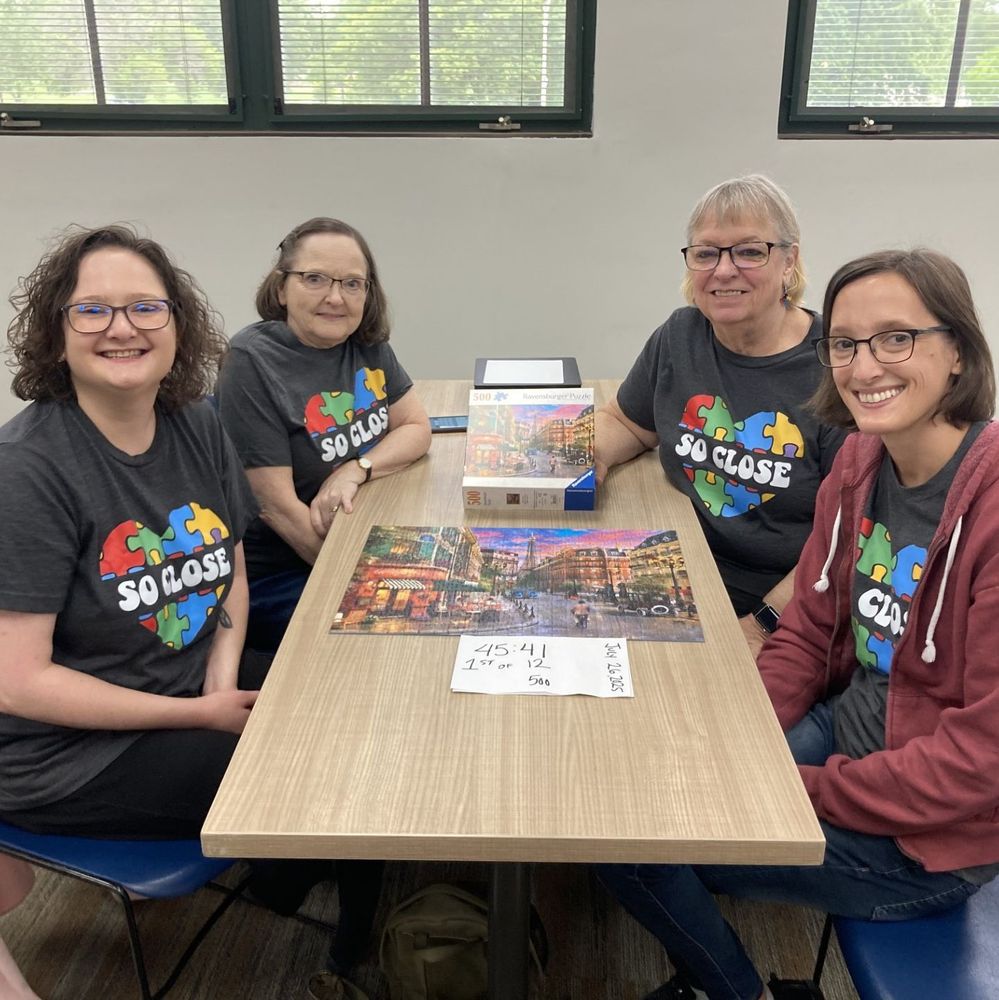 Four women sitting and smiling. On the table is their completed puzzle.
