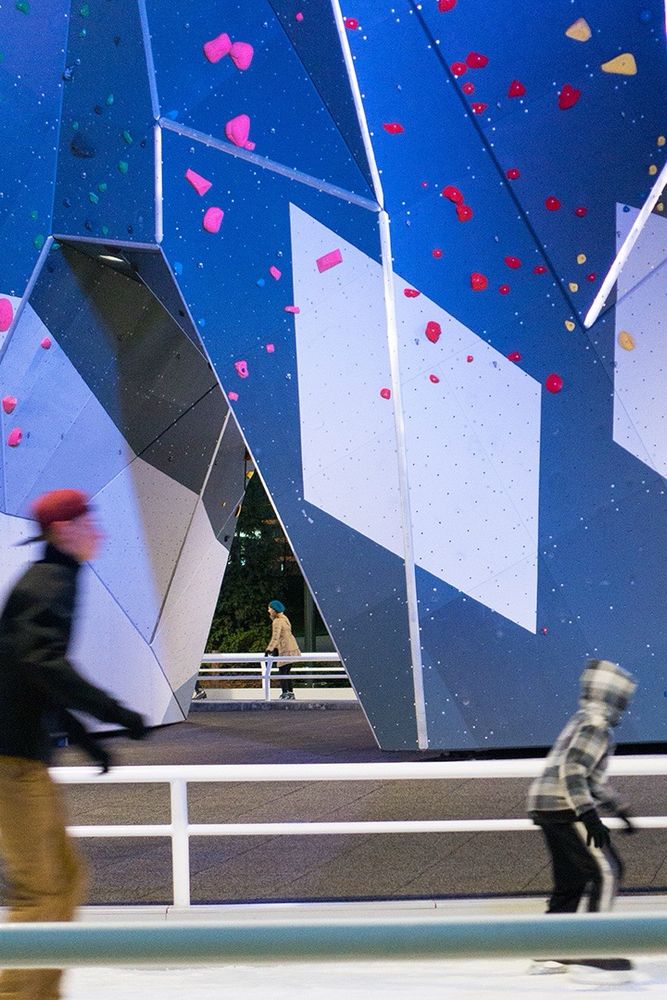 An outdoor rock climbing wall in chicago with two ice skaters in front
