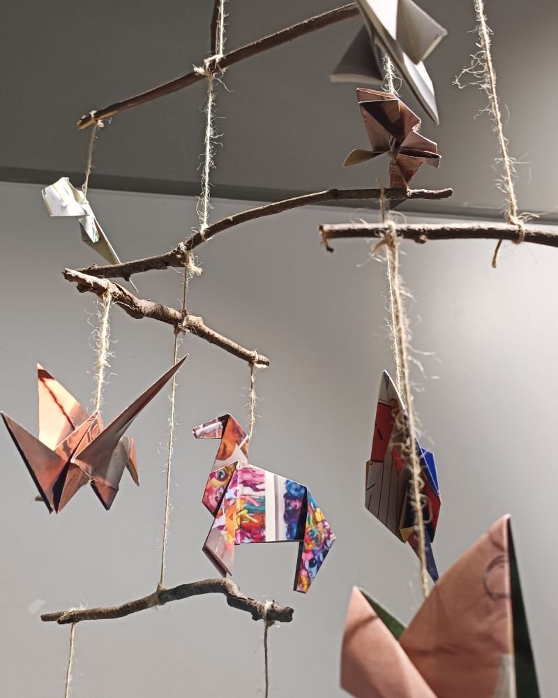 a mobile made from twigs and twine with a variety of colourful origami animals