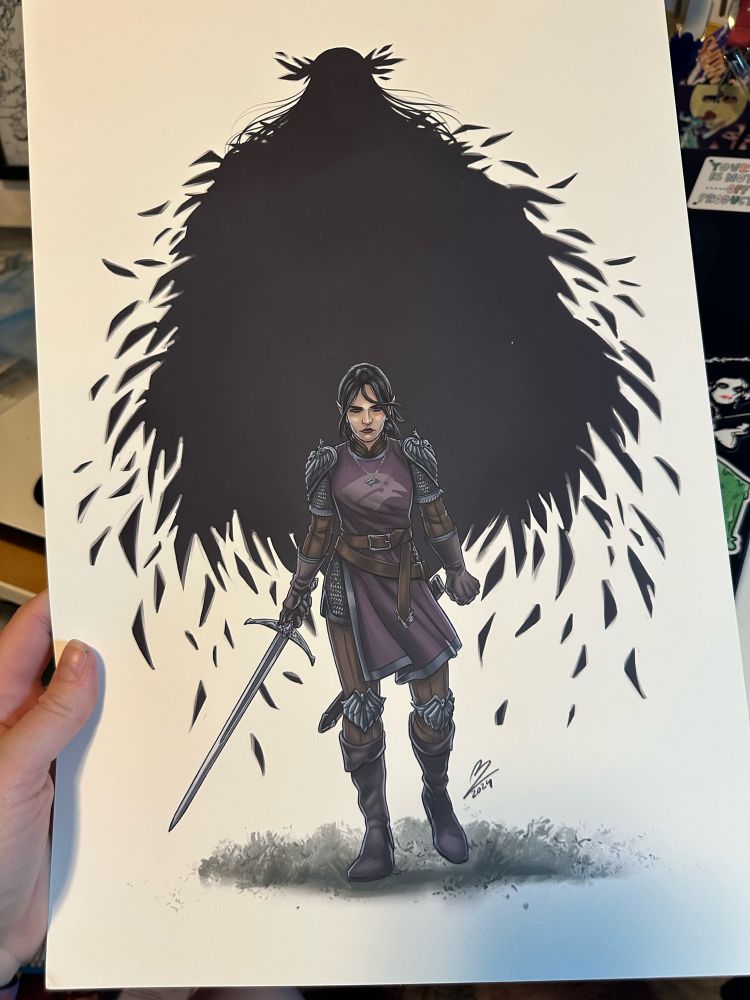 Hand holding an art print of a paladin surrounded by feathers 