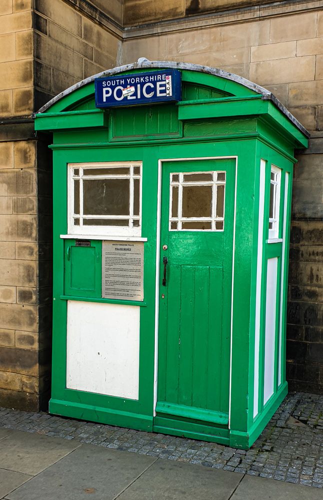 a green police phone box against a stone wall.