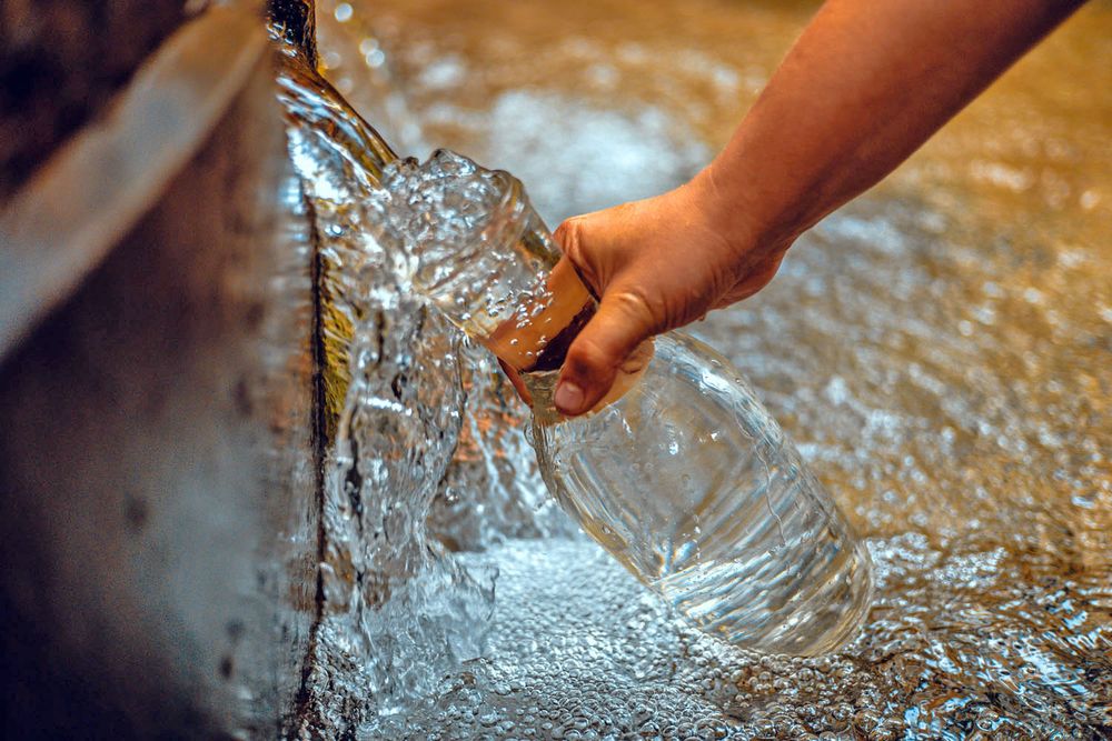 Hand füllt Glasflasche an Trinkwasserbrunnen auf.