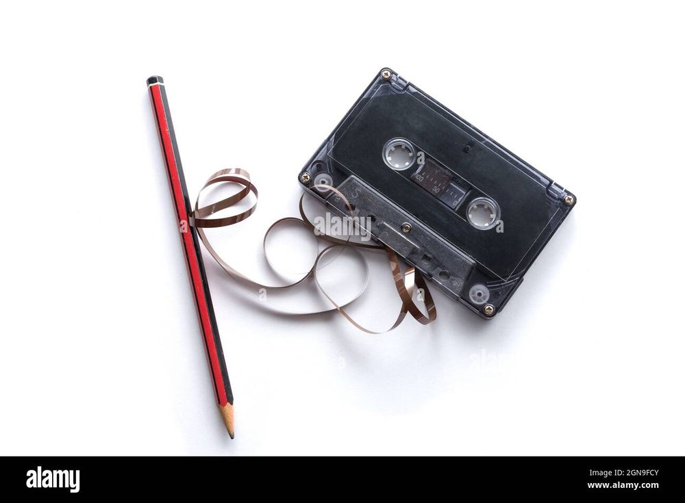 Picture of an audio cassette with spooled magnetic tape and a nearby pencil.
