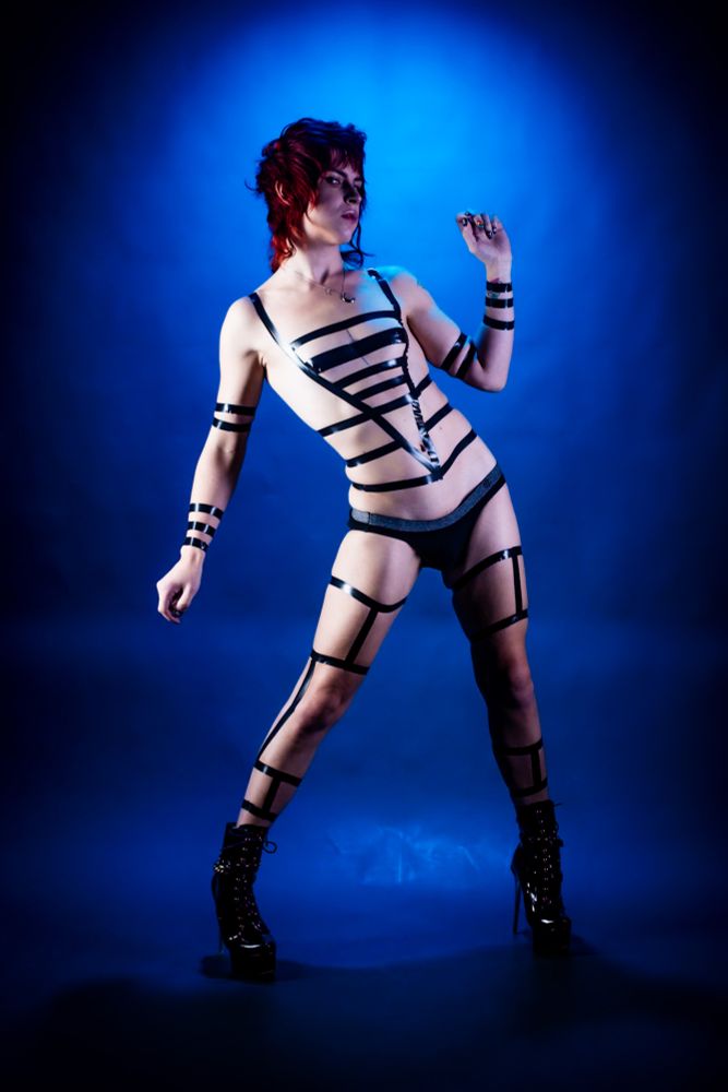 Slender sexy androgynous model with black reflective tape on their body.
Standing in high heel stilettos.
They have red hair cut pixie with a mullet