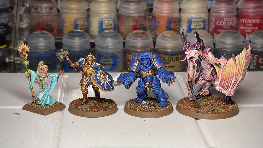 A classic metal Alarielle in flowing sky blue dress, a Stormcast Eternal, an Ultramarines Aggressor and a Tyranid Prime, painted in an ‘Eavy Metal style