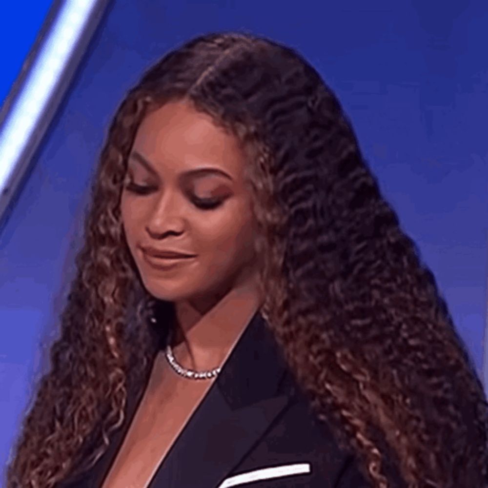 a woman with curly hair is wearing a black jacket and a necklace