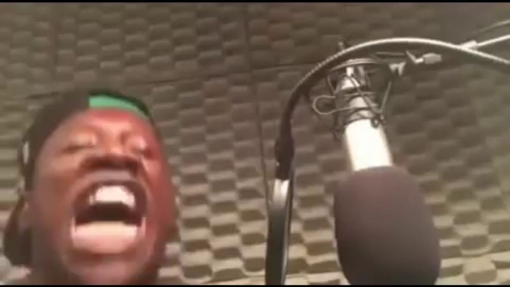 a man is singing into a microphone in a recording studio and making a funny face .