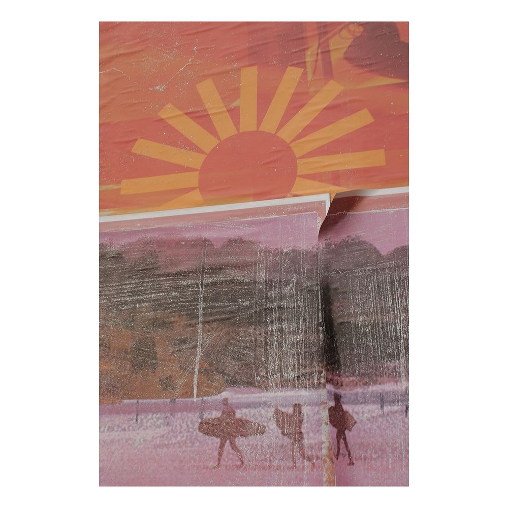 A billboard with overlapping torn posters. One has a stylised image of a glowing sun which overlaid with a low detail painting of three surfers on a beach. It's smeared and fogged with white paste.