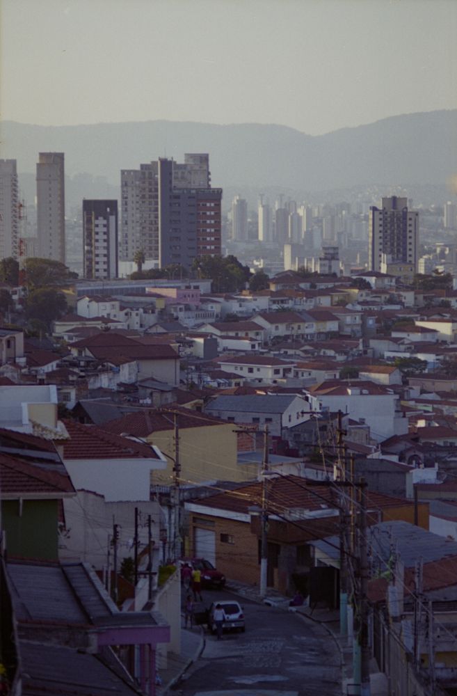 Hazy light over a big city, a small road leads into a housing quarter, high-rise buildings and mountains in the back