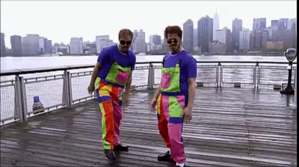 two men in colorful overalls are dancing on a pier