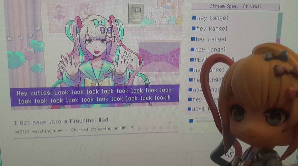 a photo taken of a OMGkawaiiangel (or simply Kangel) nendoroid figure taken in front of the game Needy Streamer Overload stream where Kangel is talking about how she's now a figure, telling the audience and the player to "look look look look look look look" so on and so forth. The nendoroid version of Kangel looks at both the stream, and the viewer, making for a somewhat meta photo considering the stream in-game is about her becoming a figure!
