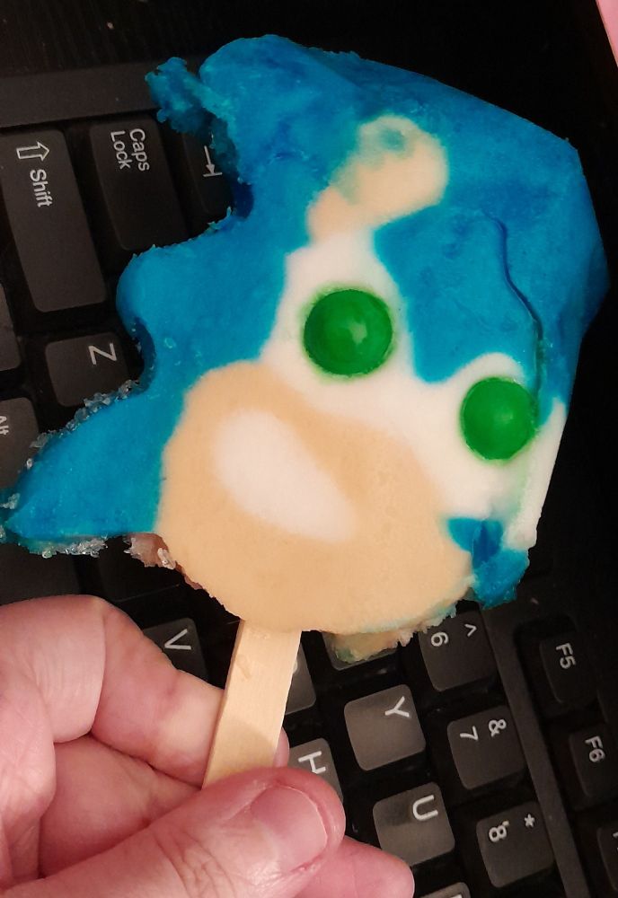 a photo of a hand holding a Sonic the Hedgehog popsicle that's head is slightly deformed, but it's green gumball eyes are perfectly aligned