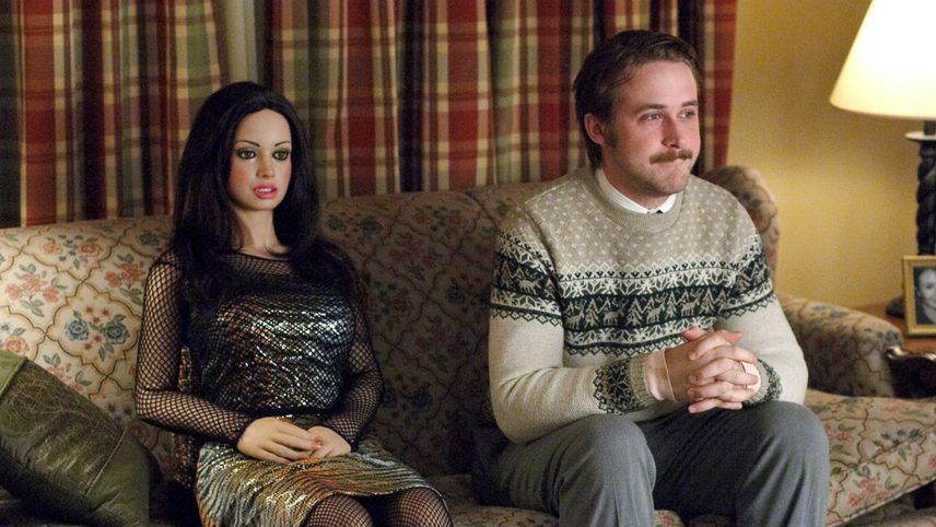 Lars sits on a sofa next to Bianca, a Real Doll that looks like a pretty young woman. 