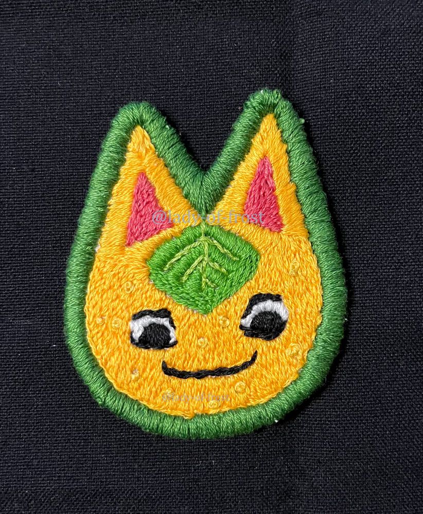 An embroidered patch of Tangy's face from Animal Crossing with a green border around her, made with long and short stitches, French knots, stem stitches, and satin stitches.