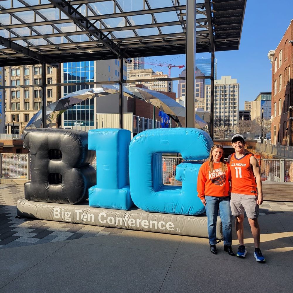 A photo of a man and woman next to an inflatable Big Ten conference sign 