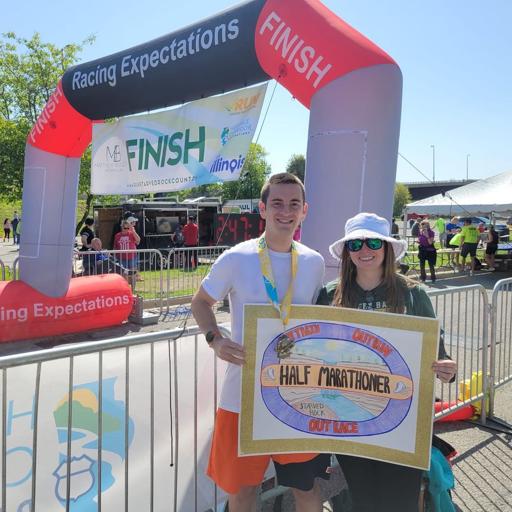 Two people at the finish line of a marathon holding a survivor-themed sign 