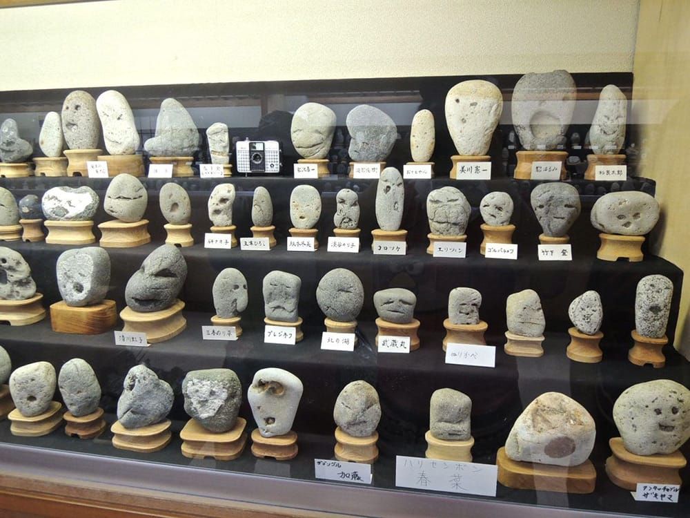 Rows of medium-sized gray rocks with various anthropomorphic "facial" expressions in a glass display case