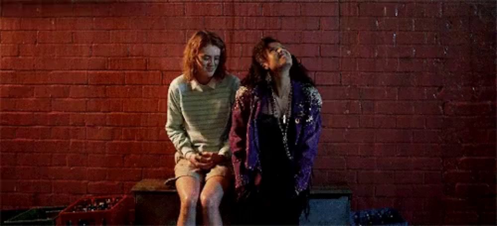 two women are sitting next to each other on a bench in front of a red brick wall .