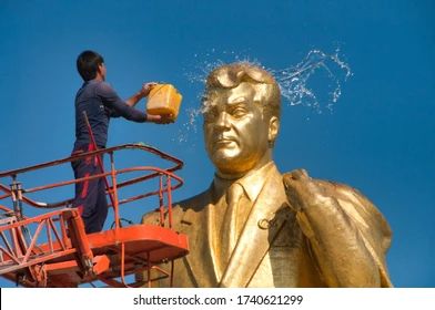 A worker, standing atop a scissor-lift, throws a bucket of water on the face of a giant gold statue of Türkmenbaşy.