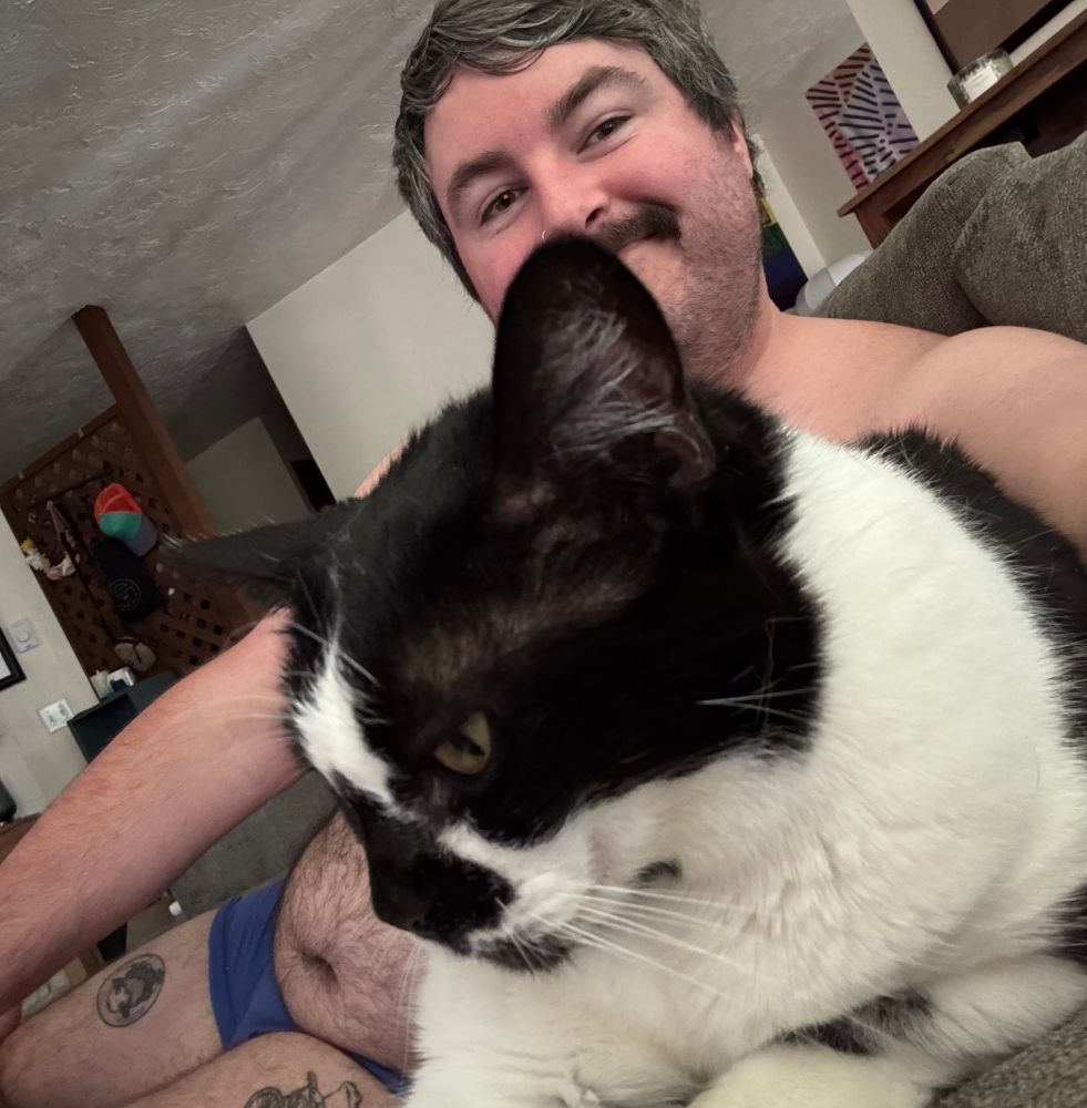 A shirtless me laying with my black and white cat