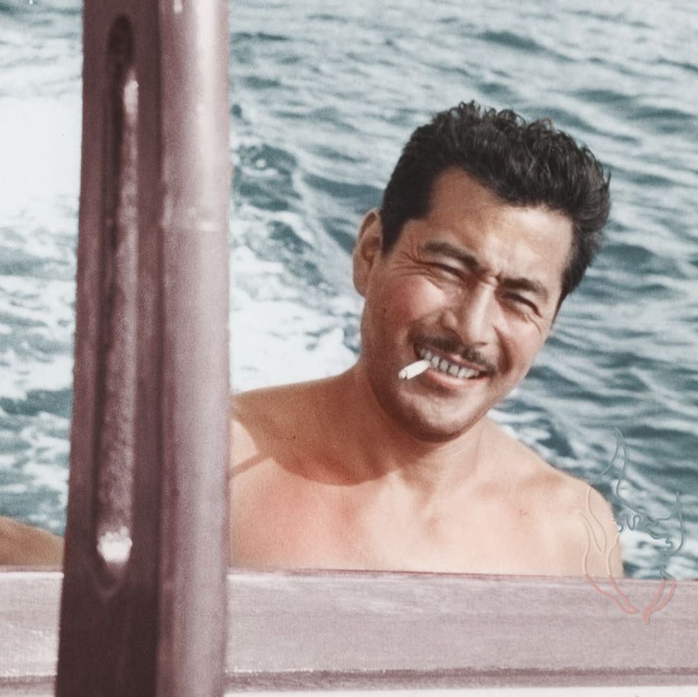 Extremely handsome Japanese actor Toshiro Mifune swimming outdoors with a cigarette in his mouth.