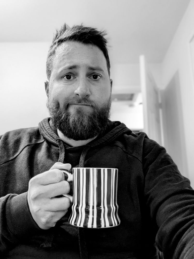 Selfie in monochrome with mug of tea. Very pronounced dimple on one side of face.
