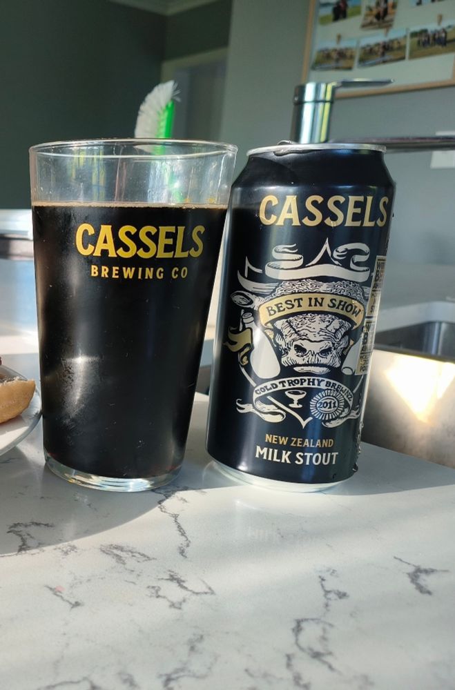 A beer glass filled with Cassels Milk Stout, next to it's can reading "Cassels Best in show New Zealand Milk Stout"