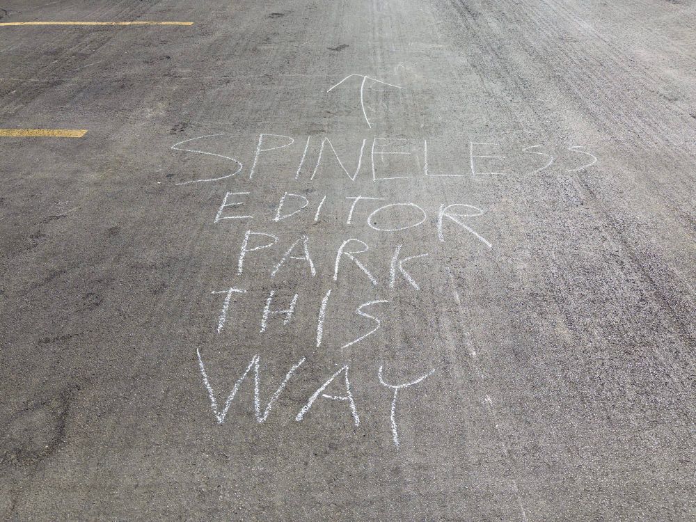 “SPINELESS EDITOR PARK THIS WAY” in chalk on pavement. 