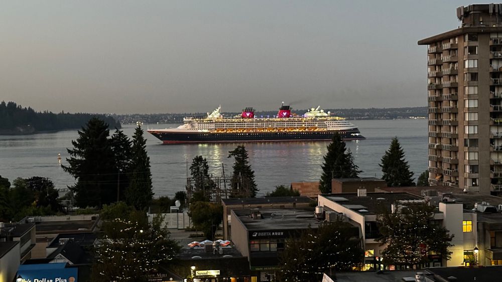 A cruise ship passing in the morning, all lit up. 
