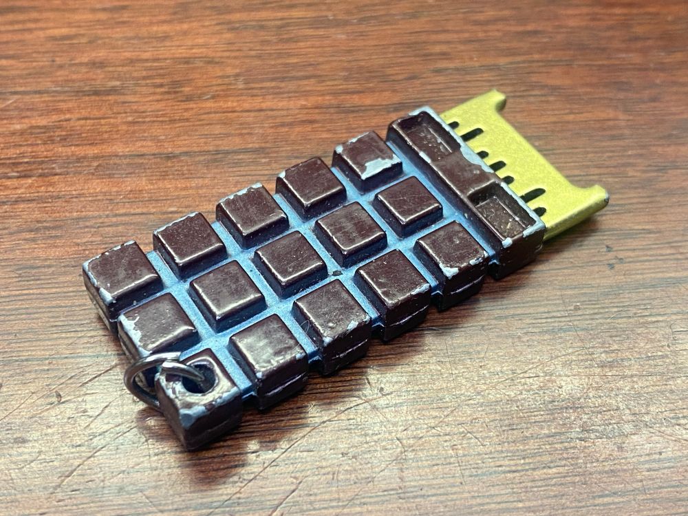 A photo of a replica of a T-800 CPU chip. It looks kind of like a small chocolate bar, with brown squares and a gold connector on one end. I carry this is in my computer bag to remind me not to trust AI. 