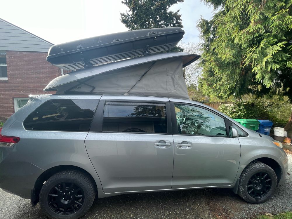 A silver Toyota Sienna van with a pop top.