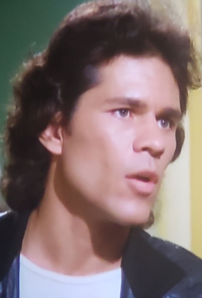 Photo of actor A Martinez in some early work in Quincy. He's sporting a mullet, and channeling The Fonz, wearing a black leather jacket over a white t shirt. He is very pretty. 