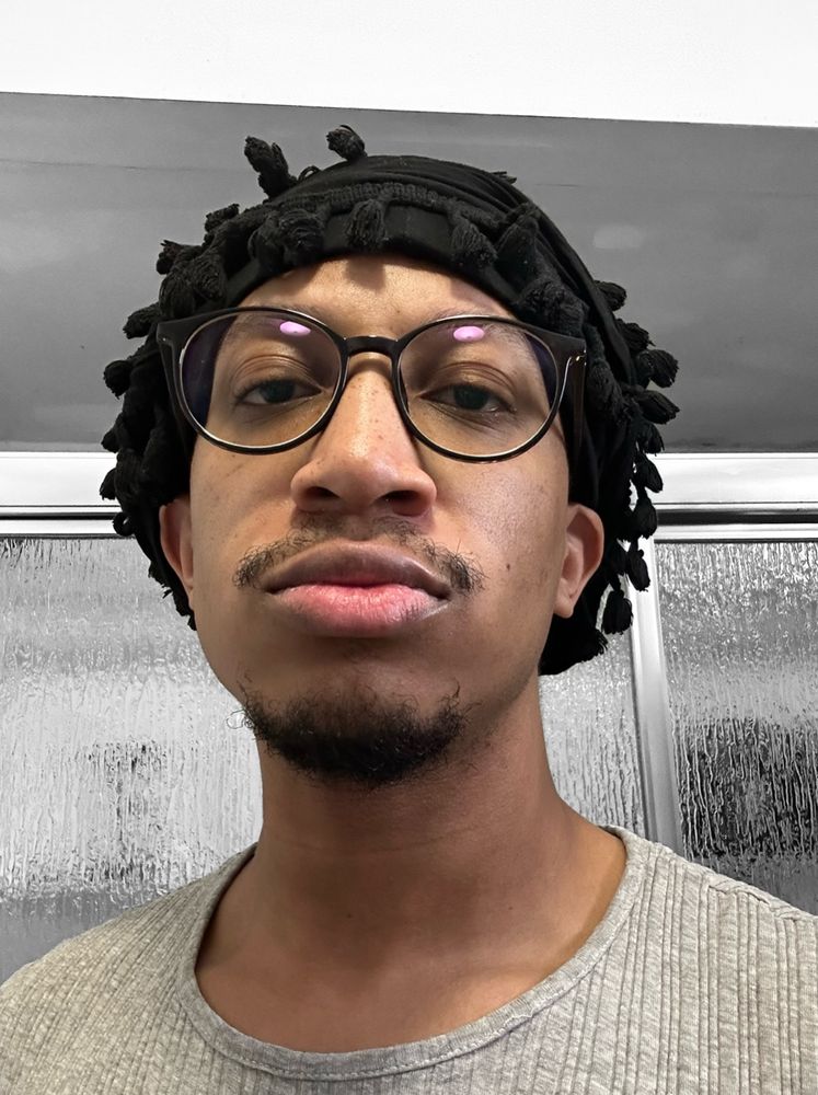 fuhtrue wearing a black head wrap, glasses and a gray ribbed shirt. 