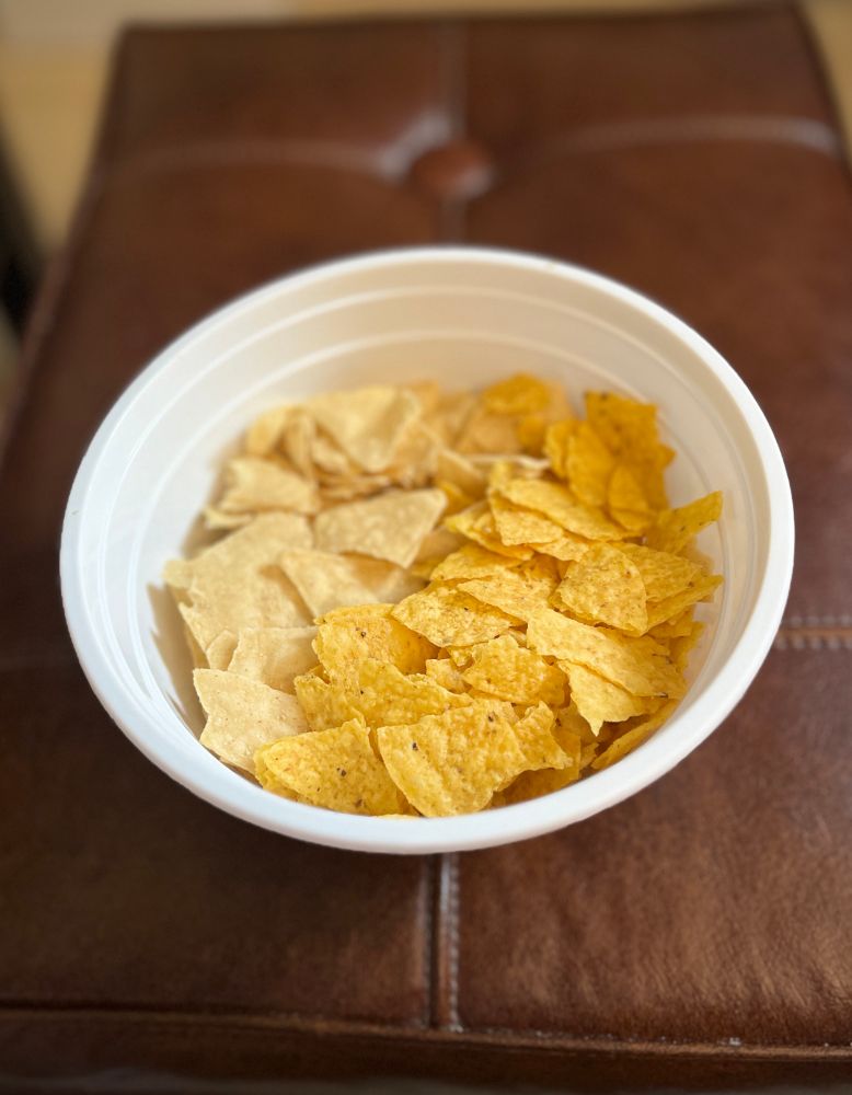 Brown background, white bowl. Two toned crunchy snack. One half is a light cream white colour and the other is a yellow orange colour. 