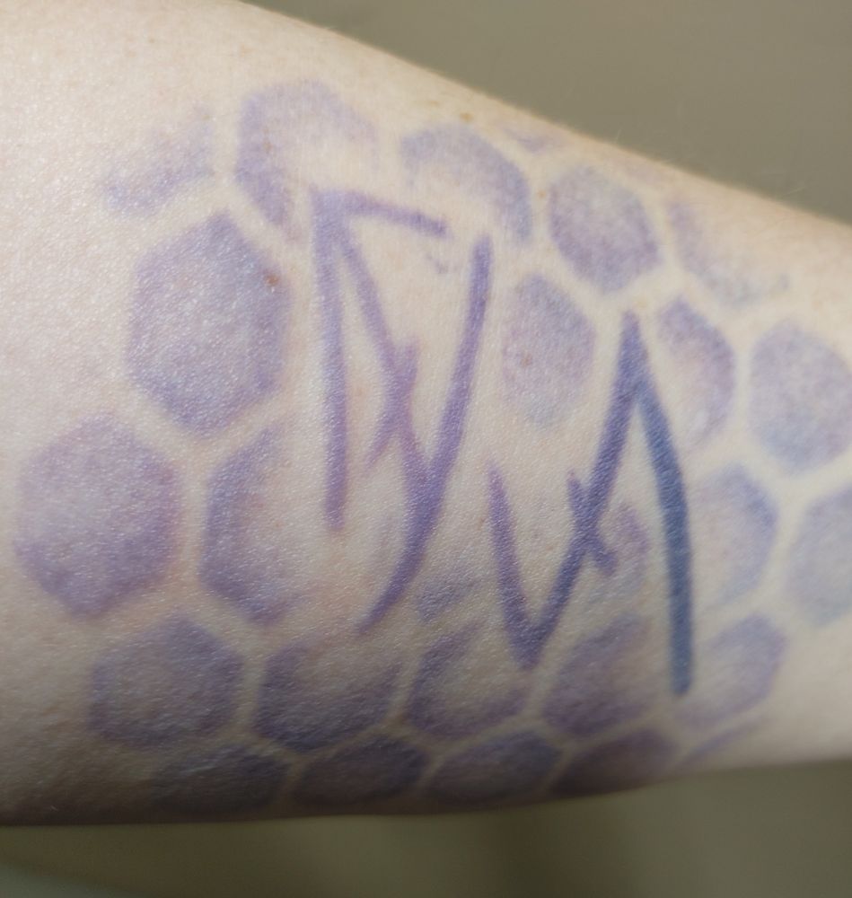 A purple gradient tattoo (which is much more vivid in person) of the feruchemical symbols for Lerasium and Pewter, against a background of hexagons, on my inner forearm. Lerasium as it's the metal of transformation, pewter for strength, in feruchemical form as representing that these come from within.