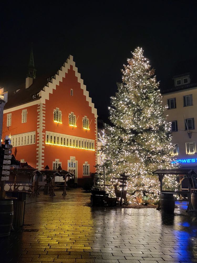 Ein rotes gotisches Rathaus mit Stufengiebel, rechts ein erleuchteten größer Christbaum, bei Nacht