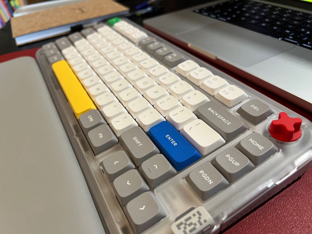 A Nuphy Kick 75 keyboard on a red mat on a desk