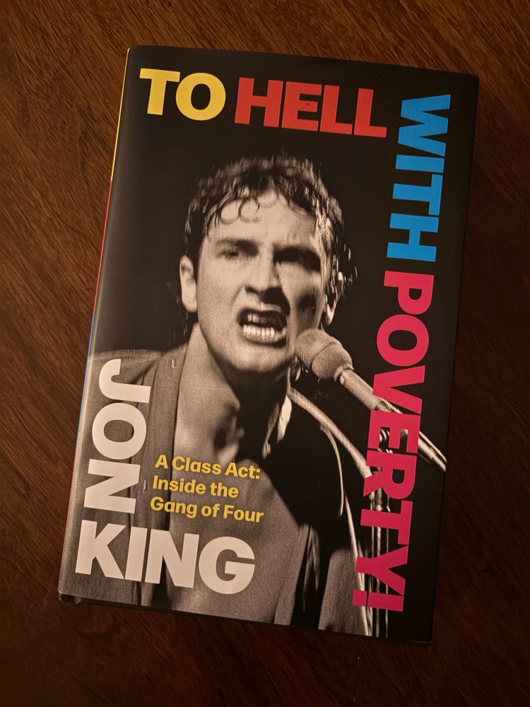 The cover of the book, “To Hell With Poverty.” The text is superimposed on a photo of Jon King’s face, taken during a performance by Gang of Four 