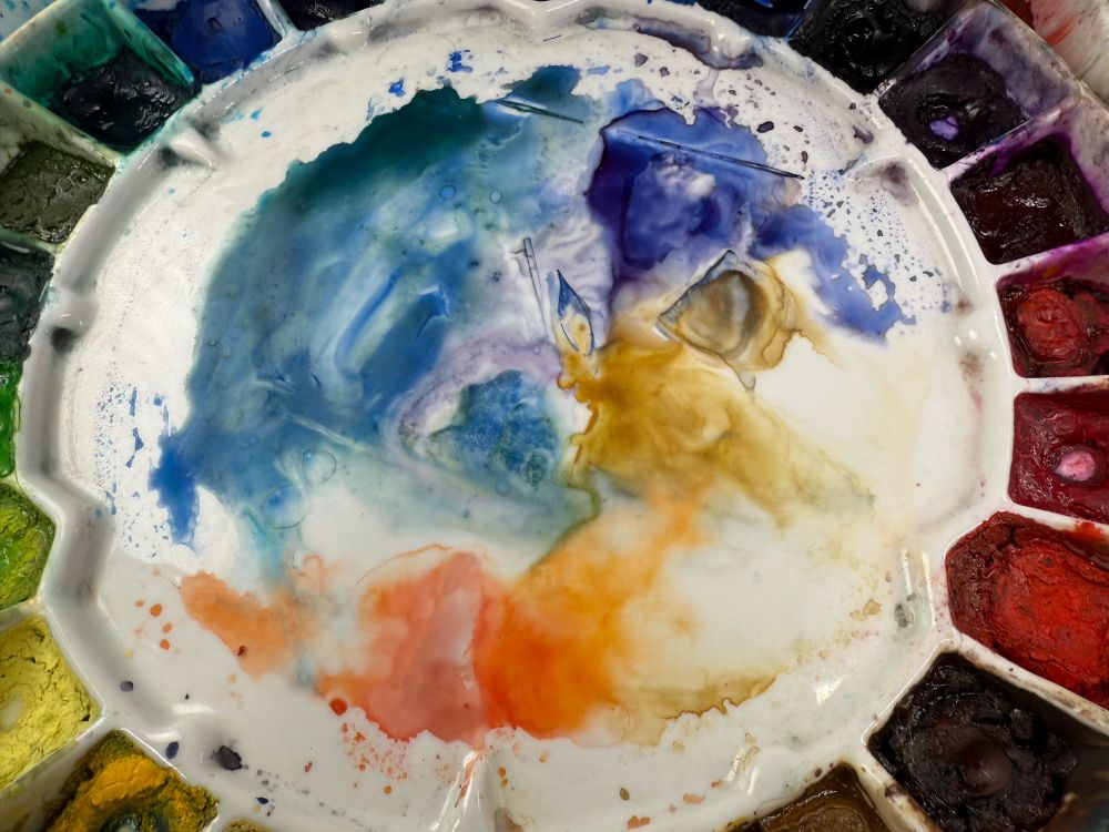 Photo of a used watercolor palette, with multiple colors bleeding into each other.