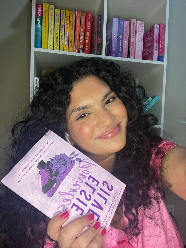 Nesta foto estou usando uma blusa rosa e estou segurando o livro Powerless da autora canadense Elsie Silver