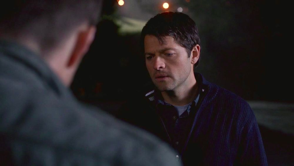 Castiel looks down at his trenchcoat, The Born-Again Identity. Dean is in the foreground. 