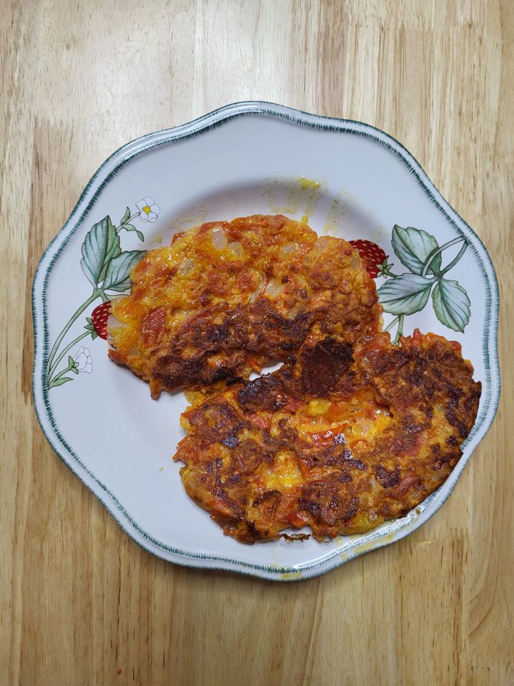 Photo of a plate holding two bean shaped fritters that vary in color from yellow to red to the brown of food fried to a moderate crispiness. 