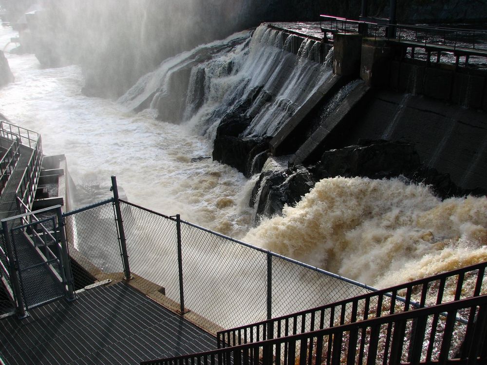 Stairs and a walkway parallel a foaming waterfall and black rocks