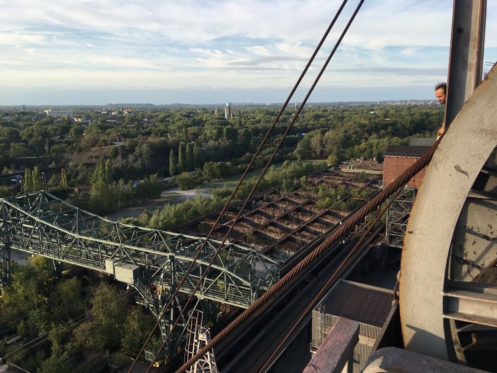 A view from the top of the blast furnace in Duisburg-Nord, showing the crane formerly used to load coke and iron ore into storage pits, plus a landscape of trees, steeples, chimneys and slag heaps beyond