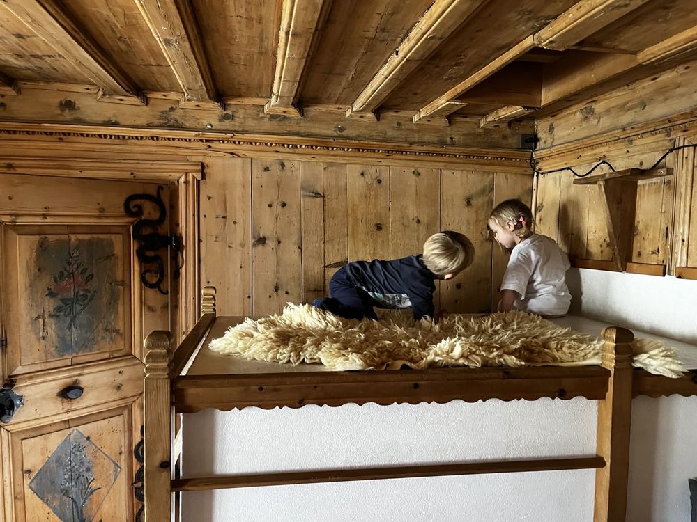 Two small kids crawling on top of a large white thermal storage unit in the corner of a wood-paneled room. Adorably, the unit has little stairs so you can easily get up and lie down on top of it. There's also a little trap door in the ceiling so you can climb up directly into the bedroom above without going through the rest of the unheated house...