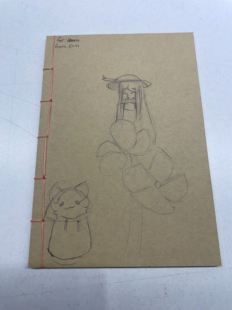 Thread-bound notebook with pink thread binding and hand-drawn art on a plain/natural background by a student for a camp teacher.