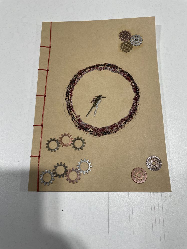 Thread-bound notebook with red thread binding and a glittery clock face with working hands and decorative metal-tone gears on a natural/brownish tone cover.