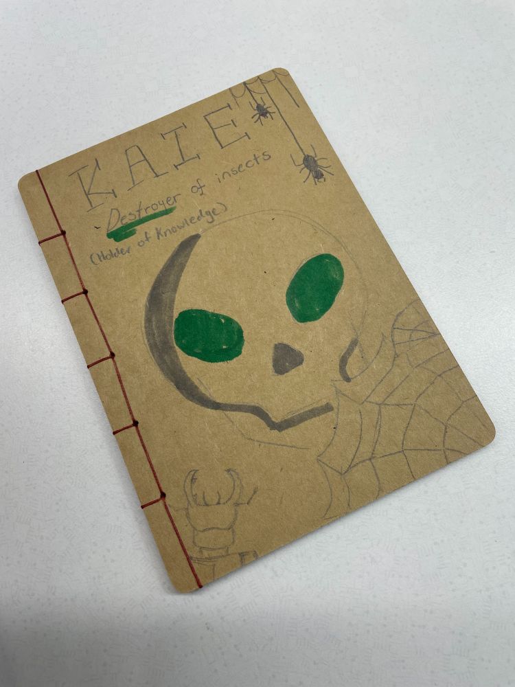 Thread-bound notebook with red thread binding and hand-drawn art on a plain/natural background by a student for a camp teacher.