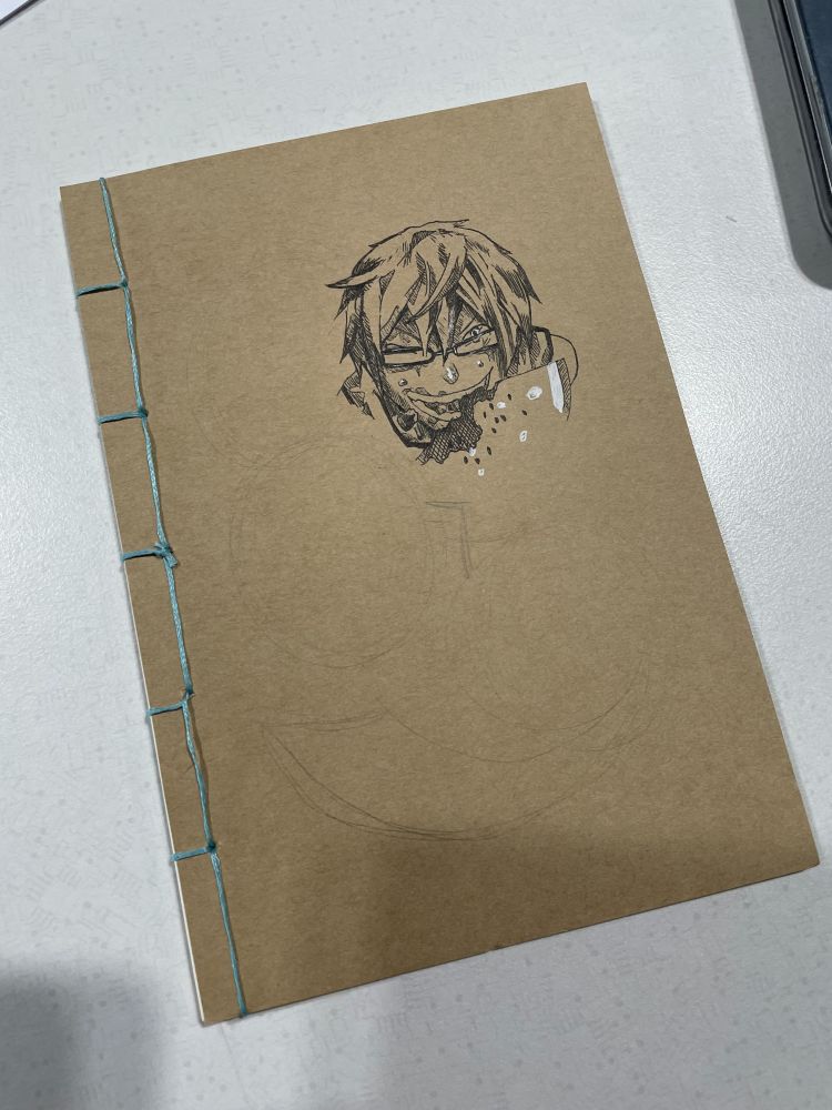 Thread-bound notebook with light blue thread and a partially inked hand-drawn anime character on a natural/brownish tone cover.